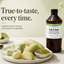 A bottle of Lorann Flavor Booster Tart & Sour fruit flavor enhancer stands on a tabletop beside a plate of pale green candy pieces, a small bowl of green gel, and lime slices. Large marketing text appears on the left, and the product bottle has a visible Lorann label.