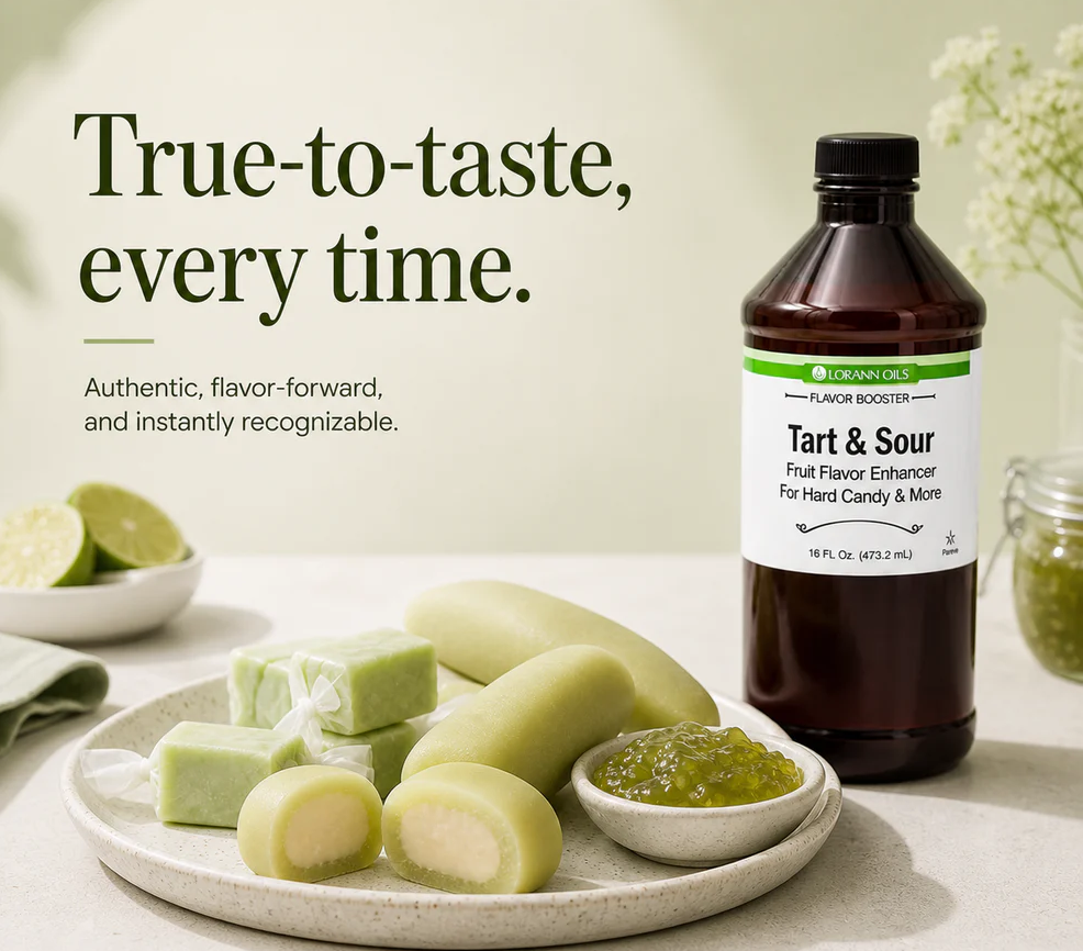 A bottle of Lorann Flavor Booster Tart & Sour fruit flavor enhancer stands on a tabletop beside a plate of pale green candy pieces, a small bowl of green gel, and lime slices. Large marketing text appears on the left, and the product bottle has a visible Lorann label.