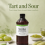 A bottle of Lorann Tart and Sour fruit flavor enhancer centered on a light green background, surrounded by green fruit, lime slices, and small bowls of the green flavoring paste. Large text at the top reads 'Tart and Sour' with the tagline 'True to taste.