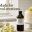 A bottle of Flavor Boosters Tart & Sour fresh flavor enhacer stands on a kitchen counter beside limes, fruit, and a decorated cake, with the text 'Made for real creations.' in the background.