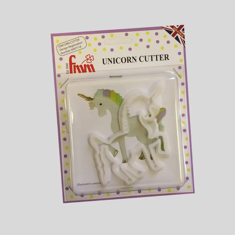 A packaged unicorn-shaped cookie cutter set in a clear blister pack with a decorative purple border. The white plastic cutter is visible inside, and the card reads 'UNICORN CUTTER' with the brand name 'fmm' shown in red.