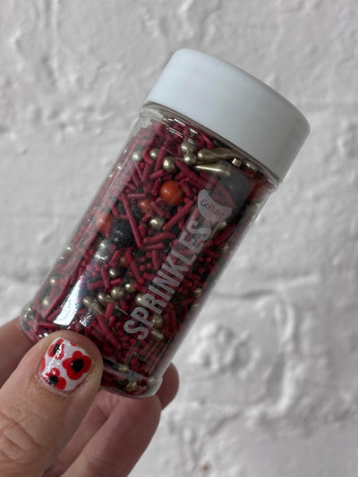 Bottle of sprinkles held by a hand with red nail polish against a white background