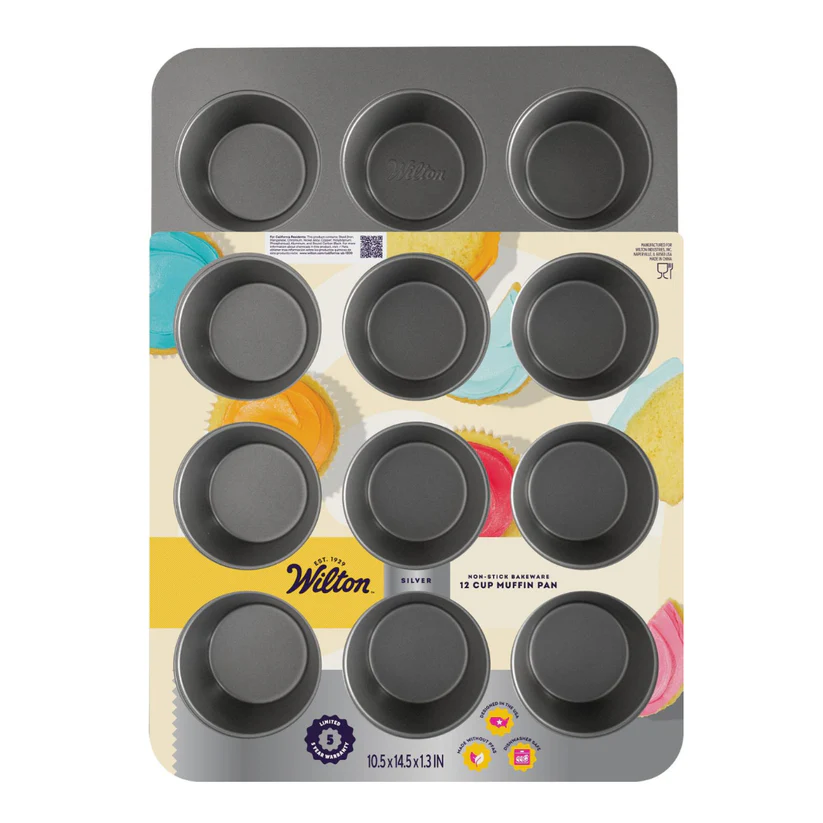A Wilton 12-cup muffin pan in dark gray, shown in its original retail packaging with a colorful printed insert card. The Wilton brand name is clearly visible on the packaging.
