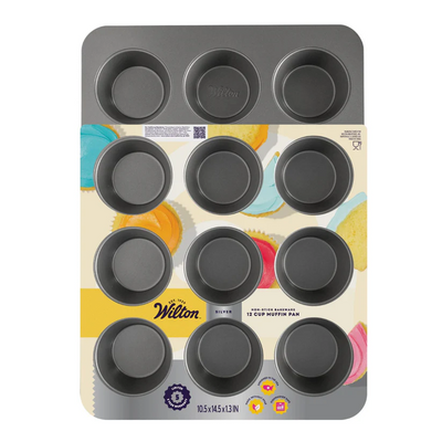 A Wilton 12-cup muffin pan in dark gray, shown in its original retail packaging with a colorful printed insert card. The Wilton brand name is clearly visible on the packaging.