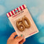 A gold glitter number candle for cakes, shaped as the number 60, held against a blue background