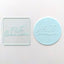 a clear acrylic debosser awith a round fondant circle  with a design that reads 'FIRST COMMUNION' , on a white background.