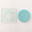 A geometric wreath with leafy branches design shown on a teal fondant icing plaque alongside a clear square acrylic debosser with the same design, placed on a white surface