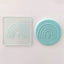 A teal fondant plaque with a rainbow and small heart design, shown beside a clear square embossing tool  featuring the same rainbow motif on a white surface.