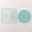 A clear embosser with the word 'Baby' imprinted on it, shown next to its blue counterpart.