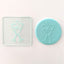 Clear acrylic debosser featuring two champagne glasses. Alongside teal fondant showing an example of use