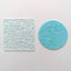 An embossing tool with floral patterns, used for imprinting designs on fondant or gumpaste icing. Alongside a blue fondant icing plaque with the same design